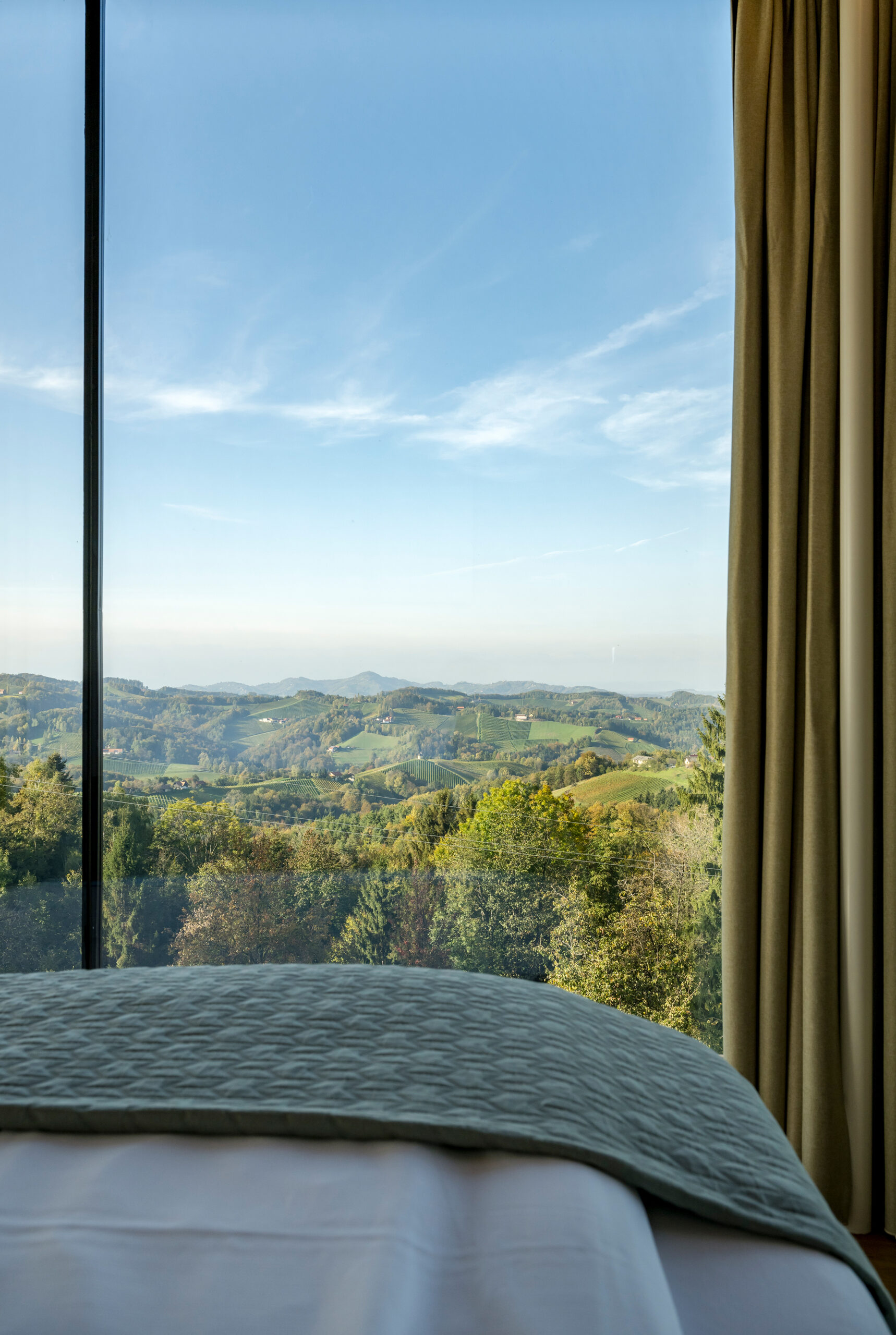 Thymianlodge Schlafzimmer — Bett mit direktem Blick über die Hügel der Südsteiermark.