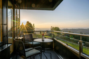 Balkon mit Tisch und zwei Sesseln im Licht der tief stehenden Sonne.